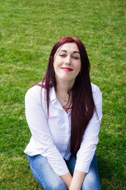 Beyaz gömlek ve mavi kot yeşil çim üzerinde oturan genç kadın