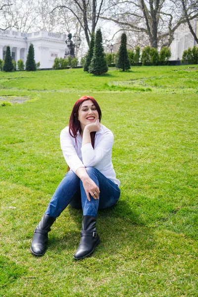 Jovem mulher de camisa branca e jeans azul sentado em uma grama verde — Fotografia de Stock