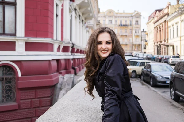 Mooie glimlachende jonge dame in zwarte vacht poseren in de stad — Stockfoto