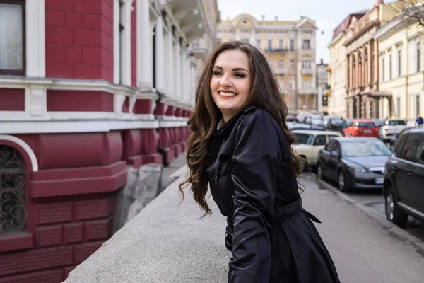 Mooie glimlachende jonge dame in zwarte vacht poseren in de stad — Stockfoto