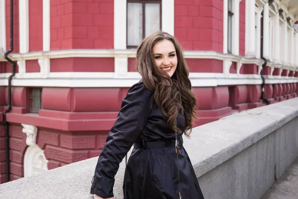 Bella sorridente giovane signora in cappotto nero in posa in città — Foto Stock