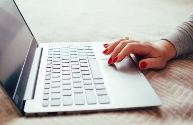 Dizüstü bilgisayarda kırmızı tırnaklı kadın eli, yatak örtüsünde dizüstü bilgisayar kullanan kadın.