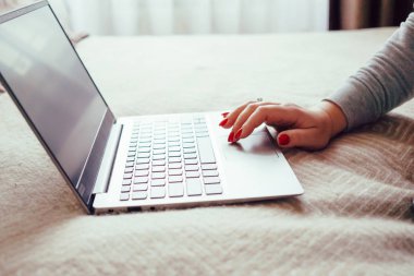 Dizüstü bilgisayarda kırmızı tırnaklı kadın eli, yatak örtüsünde dizüstü bilgisayar kullanan kadın.