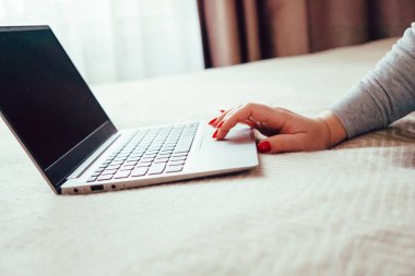 Dizüstü bilgisayarda kırmızı tırnaklı kadın eli, yatak örtüsünde dizüstü bilgisayar kullanan kadın.