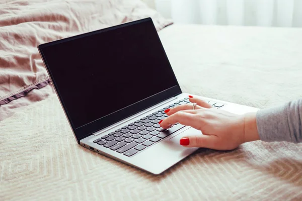 Womans hand with red nails on laptop keyboard, lady using laptop on bed blanket