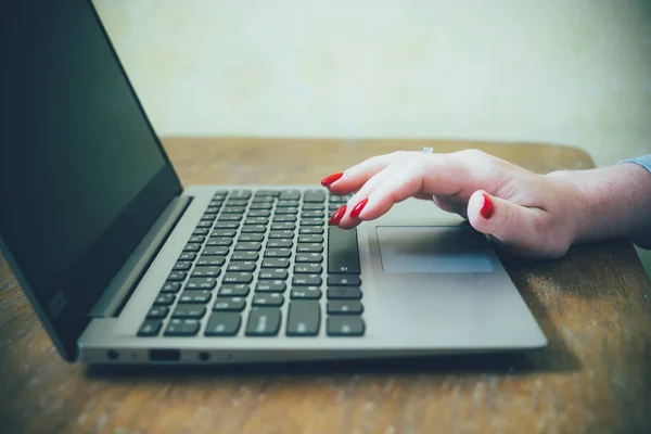 Womans hand with red nails on laptop keyboard, lady using laptop on old vintage table