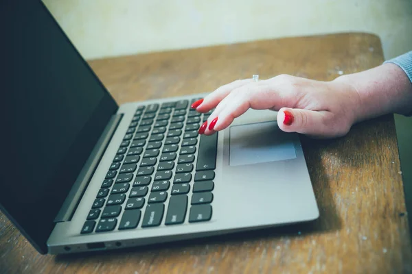 Womans hand with red nails on laptop keyboard, lady using laptop on old vintage table