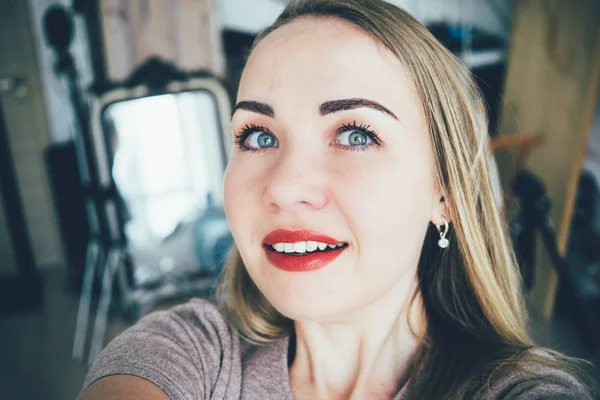 Glimlachend jong Europese blonde vrouw maakt selfie in haar Studio-appartement — Stockfoto