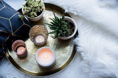 Cozy real home decoration, burning candles on golden tray with pillow on white faux fur on windowsill clipart