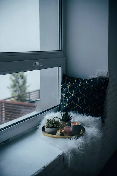 Accogliente decorazione domestica reale, candele ardenti su vassoio d'oro con cuscino su eco-pelliccia bianca sul davanzale della finestra — Foto Stock