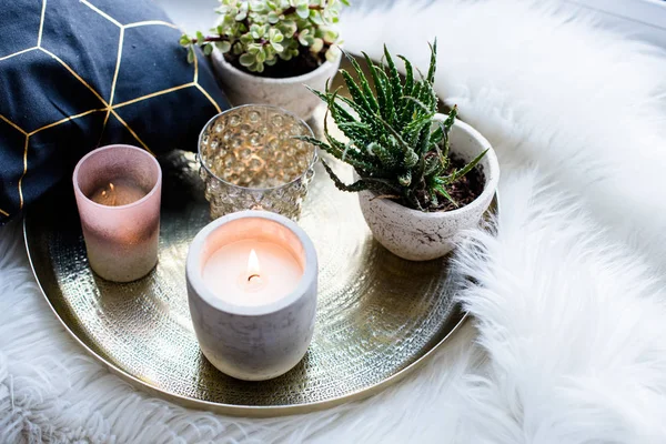Gemütliche echte Wohndekoration, brennende Kerzen auf goldenem Tablett mit Kissen auf weißem Kunstfell auf der Fensterbank — Stockfoto