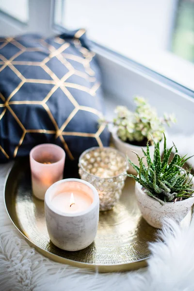 Gemütliche echte Wohndekoration, brennende Kerzen auf goldenem Tablett mit Kissen auf weißem Kunstfell auf der Fensterbank — Stockfoto