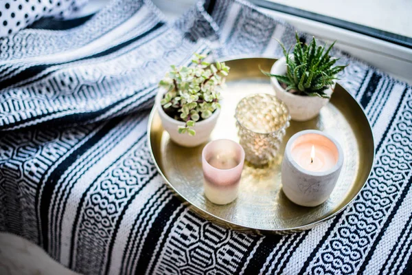 Echte Wohnungseinrichtung, aromatische Kerzen und Pflanzen auf Vintage-Tablett mit Kissen und Decke auf weißem Fensterbrett — Stockfoto