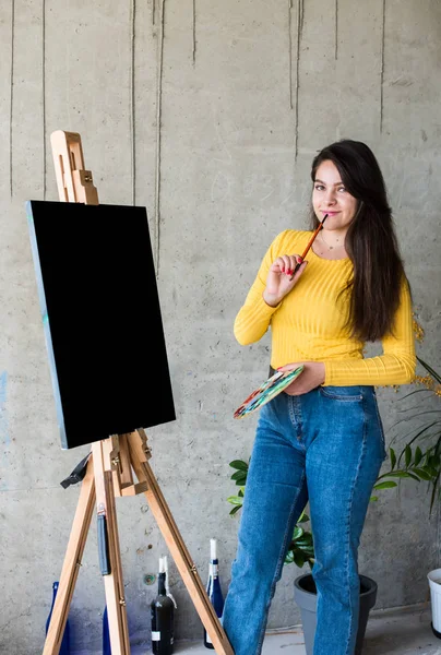 Νεαρή ζωγράφος καλλιτέχνης κυρία με απομονωμένα έργα τέχνης καμβά mock-up στο καβαλέτο — Φωτογραφία Αρχείου