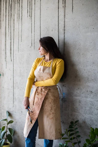 Jonge mooie dame artiest in schort met verf vlekken in haar loft artistieke studio — Stockfoto