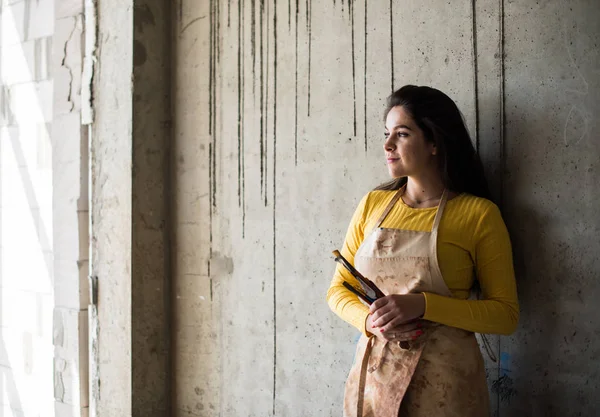 Young beautiful lady artist in apron with paint stains in her loft artistic studio