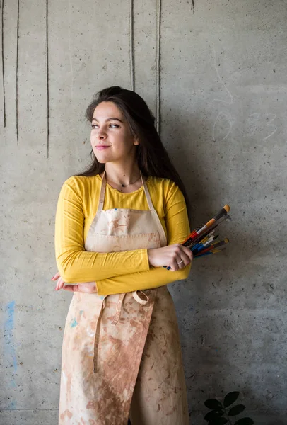 Young beautiful lady artist in apron with paint stains in her loft artistic studio — Stock Photo, Image