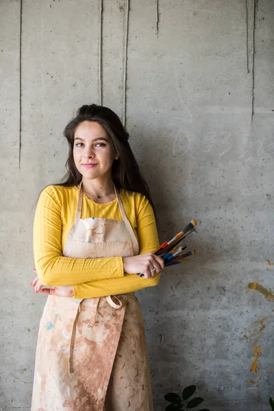 Junge schöne Künstlerin in Schürze mit Farbflecken in ihrem künstlerischen Atelier auf dem Dachboden — Stockfoto