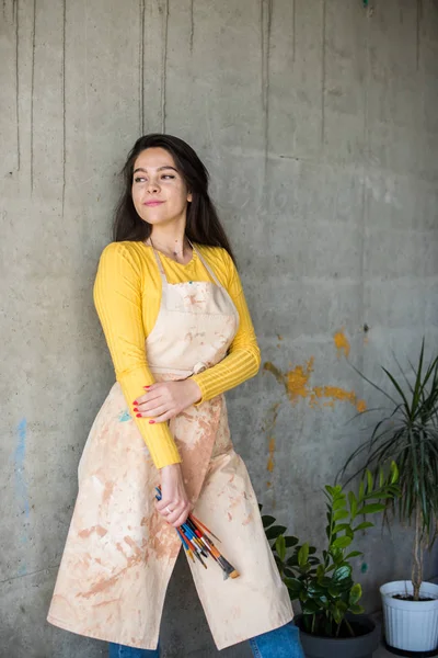 Jovem bela senhora artista em avental com manchas de tinta em seu estúdio artístico loft — Fotografia de Stock