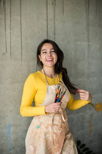 Jonge mooie dame artiest in schort met verf vlekken in haar loft artistieke studio — Stockfoto