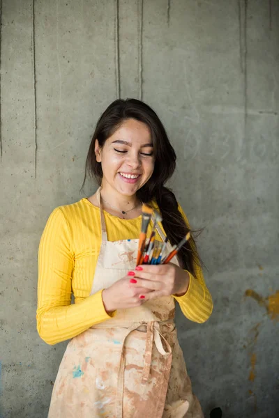 Jeune belle dame artiste en tablier avec des taches de peinture dans son studio artistique loft — Photo