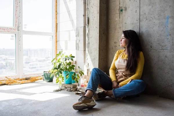 Giovane bella signora artista in grembiule con macchie di vernice seduta sul pavimento nel suo studio — Foto Stock
