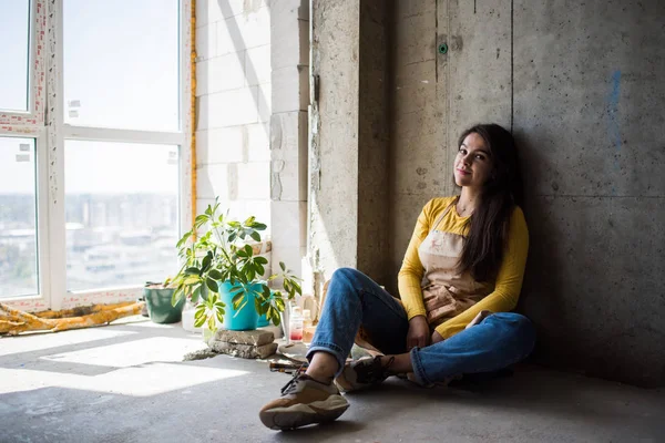 Junge schöne Künstlerin in Schürze mit Farbflecken auf dem Boden in ihrem Atelier — Stockfoto