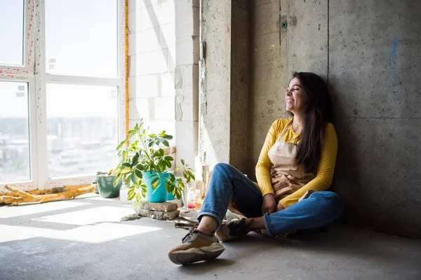 Jonge mooie dame artiest in schort met verf vlekken zitten op de vloer in haar studio — Stockfoto