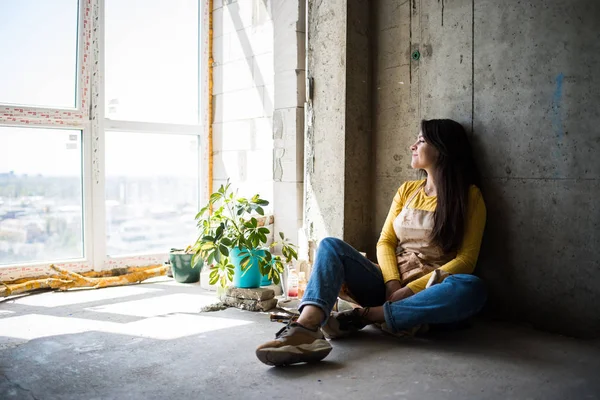 Jonge mooie dame artiest in schort met verf vlekken zitten op de vloer in haar studio — Stockfoto