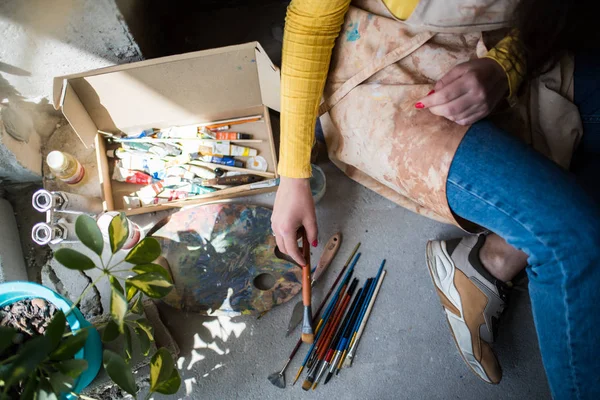 Young beautiful lady artist in apron with paint stains sitting on the floor in her studio — 스톡 사진