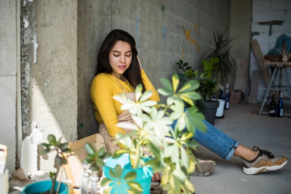 Ung vacker dam konstnär i förkläde med färg fläckar sitter på golvet i sin studio — Stockfoto