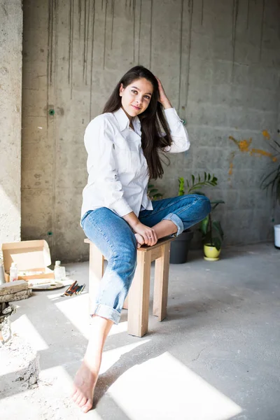 Mooie jonge dame kunstenaar in wit shirt zittend blootsvoets in haar Boheemse artistieke Studio loft — Stockfoto