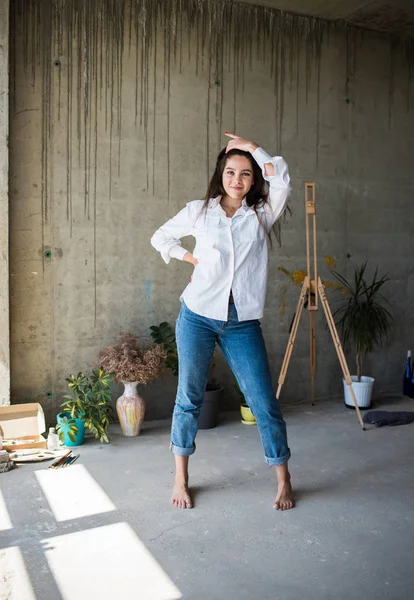 Mooie jonge dame kunstenaar in wit overhemd dansen blootsvoets in haar Boheemse artistieke Studio loft — Stockfoto