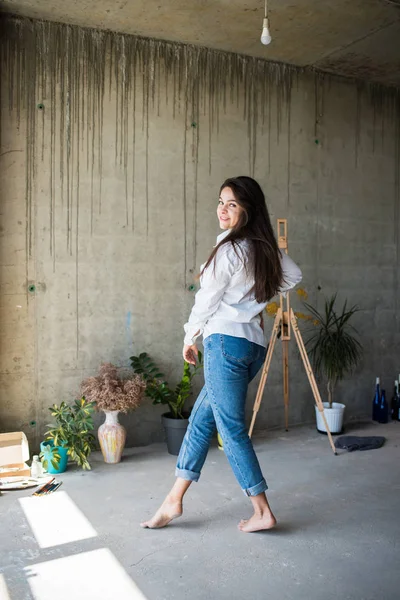 Mooie jonge dame kunstenaar in wit overhemd dansen blootsvoets in haar Boheemse artistieke Studio loft — Stockfoto