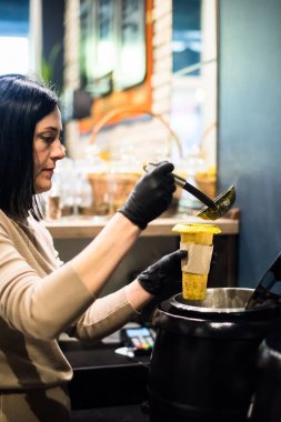 Genç bayan mutfak işçisi bardağa çorba dolduruyor. 
