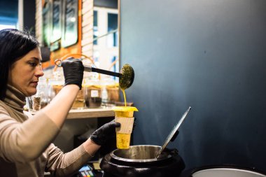 Genç bayan mutfak işçisi bardağa çorba dolduruyor. 