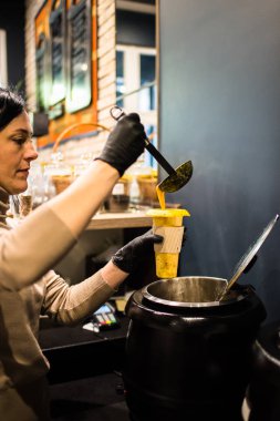 Genç bayan mutfak işçisi bardağa çorba dolduruyor. 