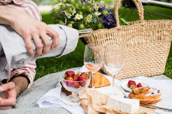 Mans hand pouring rose wine into glasses, summer picnic