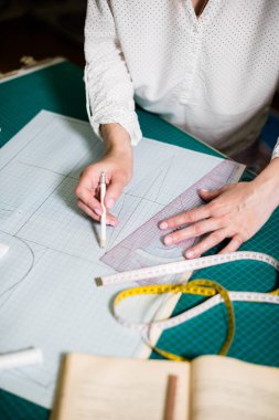 Atölyesinde çalışan bayan terzinin elleri, dikiş masasında ki alet ve kumaş örnekleri
