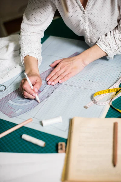 Manos de señora sastre trabajando en su estudio, herramientas y muestras de tela en la mesa de coser — Foto de Stock