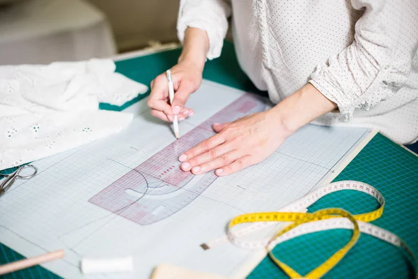 Mãos de senhora alfaiate trabalhando em seu estúdio, ferramentas e amostras de tecido na mesa de costura — Fotografia de Stock