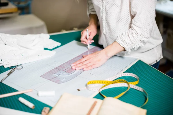 Manos de señora sastre trabajando en su estudio, herramientas y muestras de tela en la mesa de coser — Foto de Stock