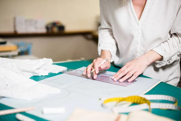 Mãos de senhora alfaiate trabalhando em seu estúdio, ferramentas e amostras de tecido na mesa de costura — Fotografia de Stock