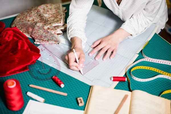 Mani di sarto signora che lavorano nel suo studio, strumenti e campioni di tessuto sul tavolo da cucito — Foto Stock