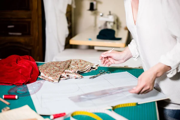 Handen van Lady Tailor werken in haar atelier, gereedschap en stof stalen op de naai tafel — Stockfoto