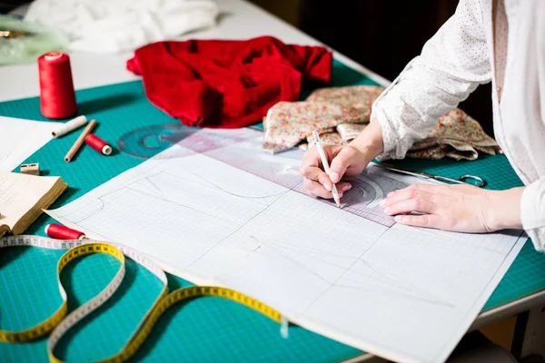 Hands of lady tailor working in her studio, tools and fabric samples on the sewing table — Stock Photo, Image