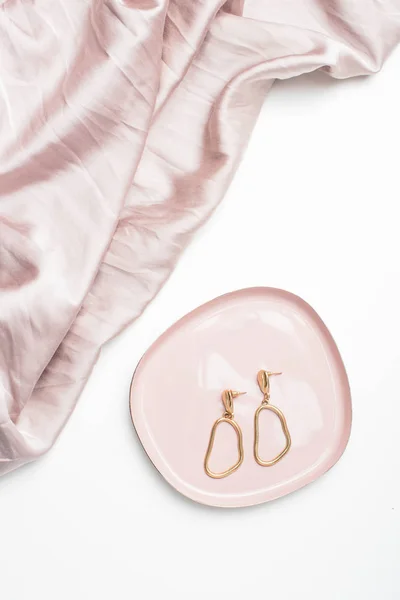 Boucles d'oreilles dorées sur plaque à bijoux en tissu de soie beige — Photo