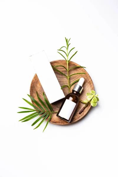 Brown glass cosmetic bottle mock-up with blank white label and green leaves, serum packaging — Stock Photo, Image