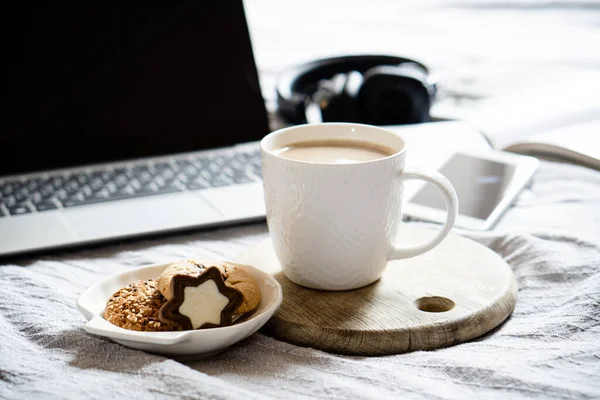 Real home workplace, laptop with cup of coffee with cookies on bed with cozy blanket