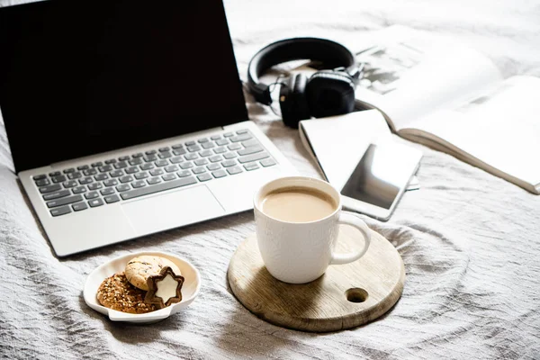 Настоящее домашнее рабочее место, ноутбук с чашкой кофе с кулинарией на кровати с уютным одеялом — стоковое фото